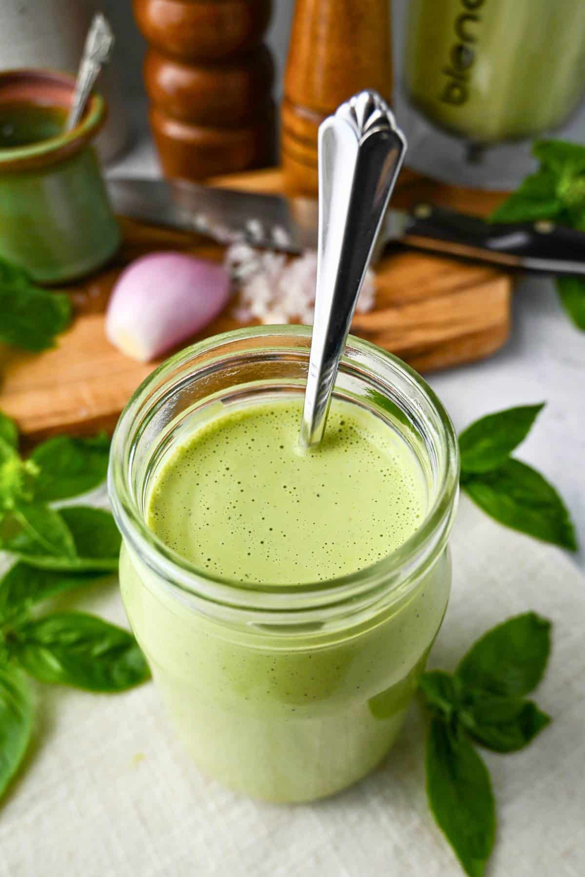 a jar of green goddess dressing with a spoon with a shallot behind it
