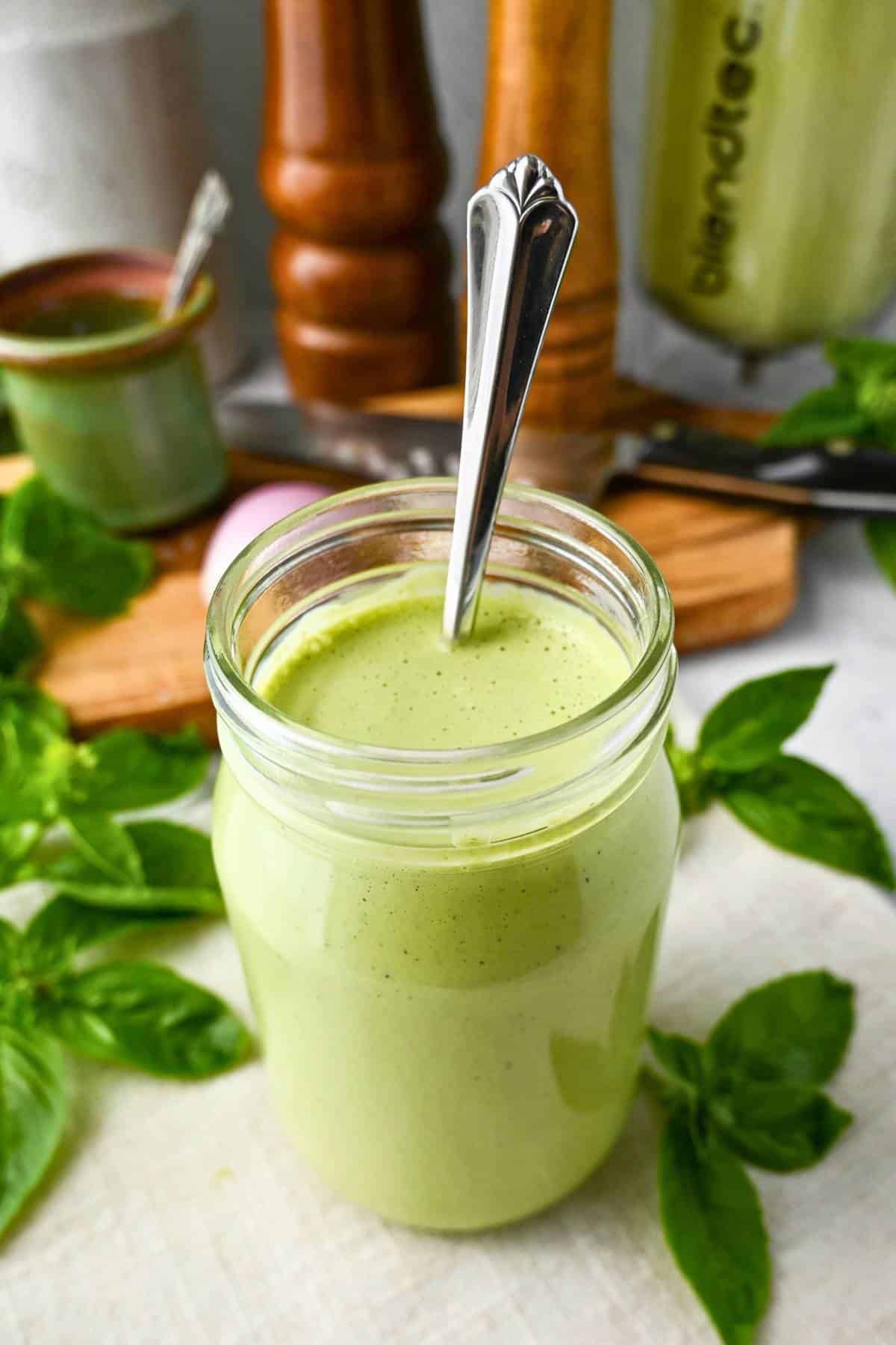 a jar of green goddess with a spoon with a salt and pepper shaker behind it