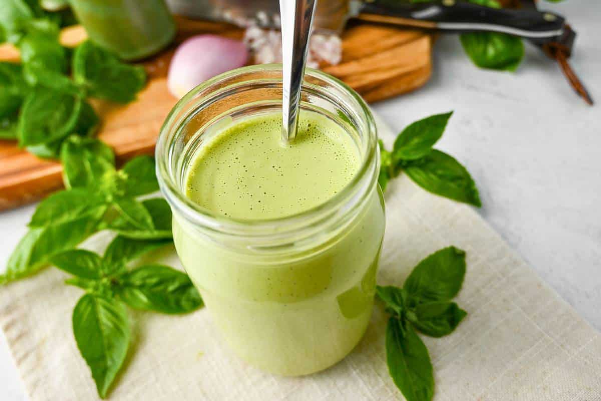 a jar of creamy basil dressing surrounded by fresh basil